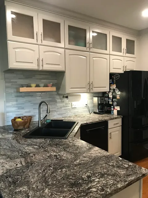 White kitchen cabinets with blue backsplash and granite island countertop