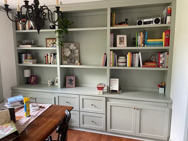 Sage green built-in shelving with desk, lower cabinets and brass hardware