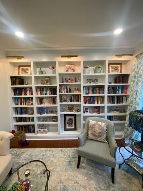 Floor-to-ceiling white built-in bookcase with illuminated shelves and storage