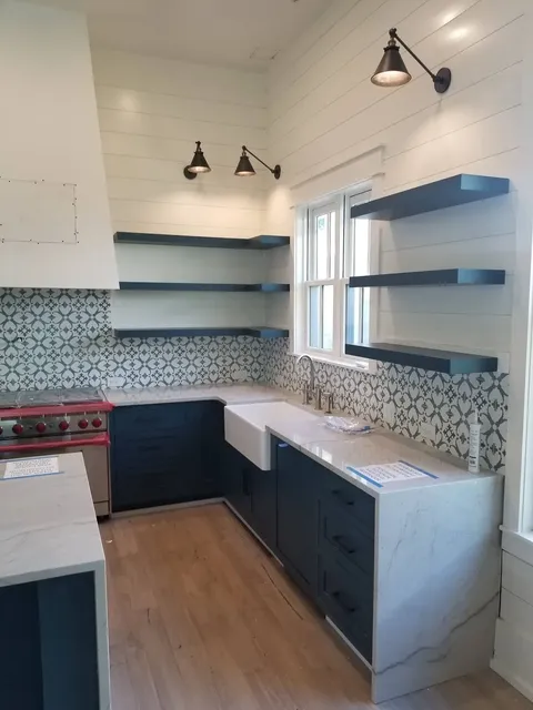 Dark blue kitchen cabinets with white marble countertops and open shelving