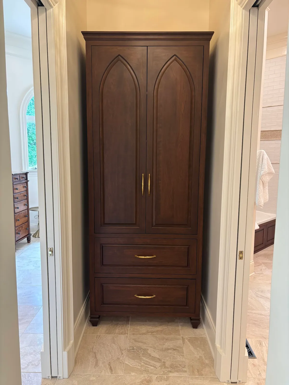 Tall dark stained armoire with arched doors and brass hardware