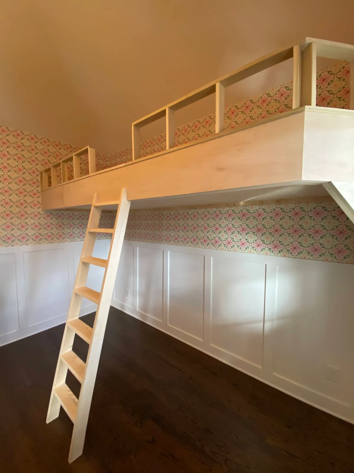Custom loft bunk bed with natural wood railings and floral wallpaper