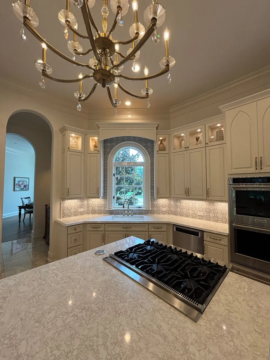 Cream kitchen with granite island, arched window, and brass chandelier