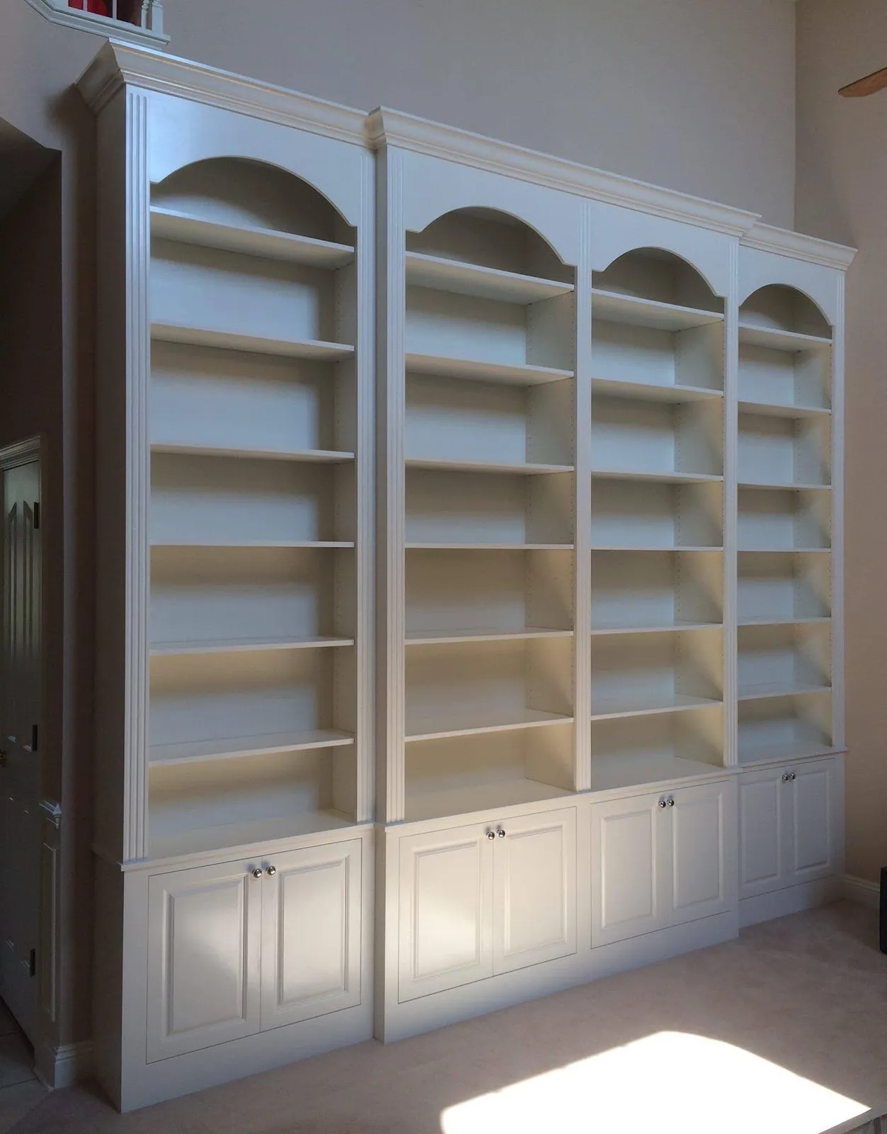 White built-in bookcase wall with arched top shelving and cabinet storage