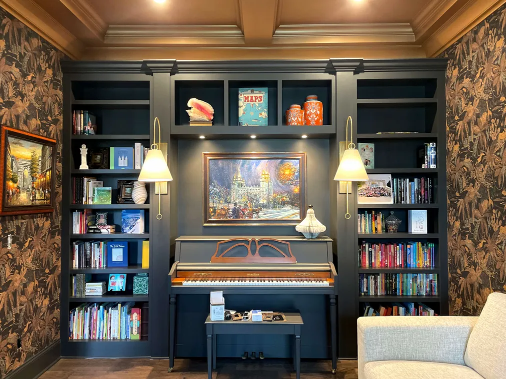 Dark blue library wall with built-in shelving and brass pendant lights