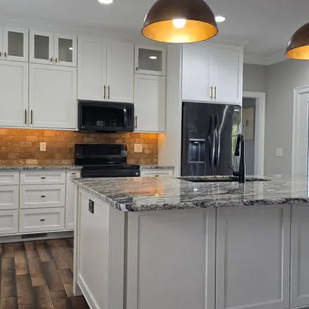 White kitchen cabinets with orange tile backsplash and granite island