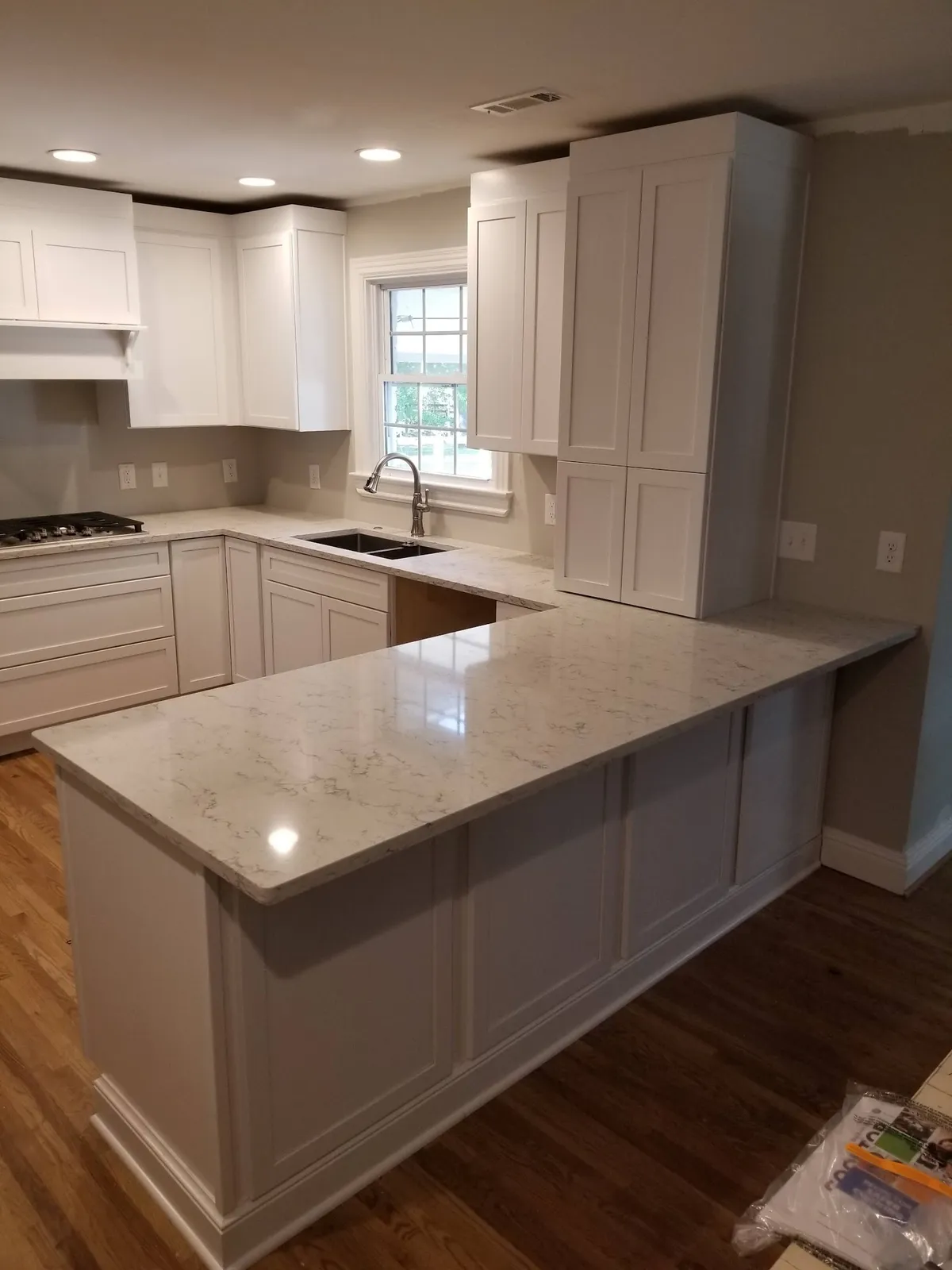 Cream kitchen with large marble island, white cabinets and wall shelves