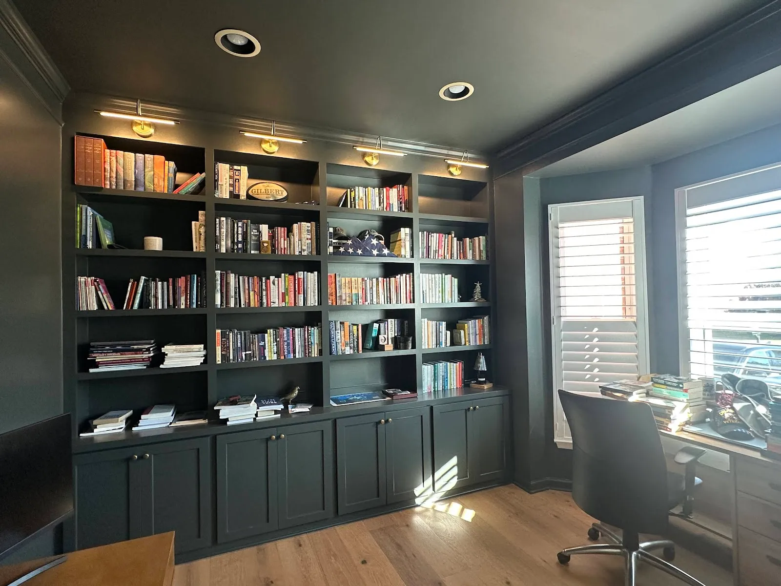 Dark teal library shelving with glass-front upper cabinets and brass hardware