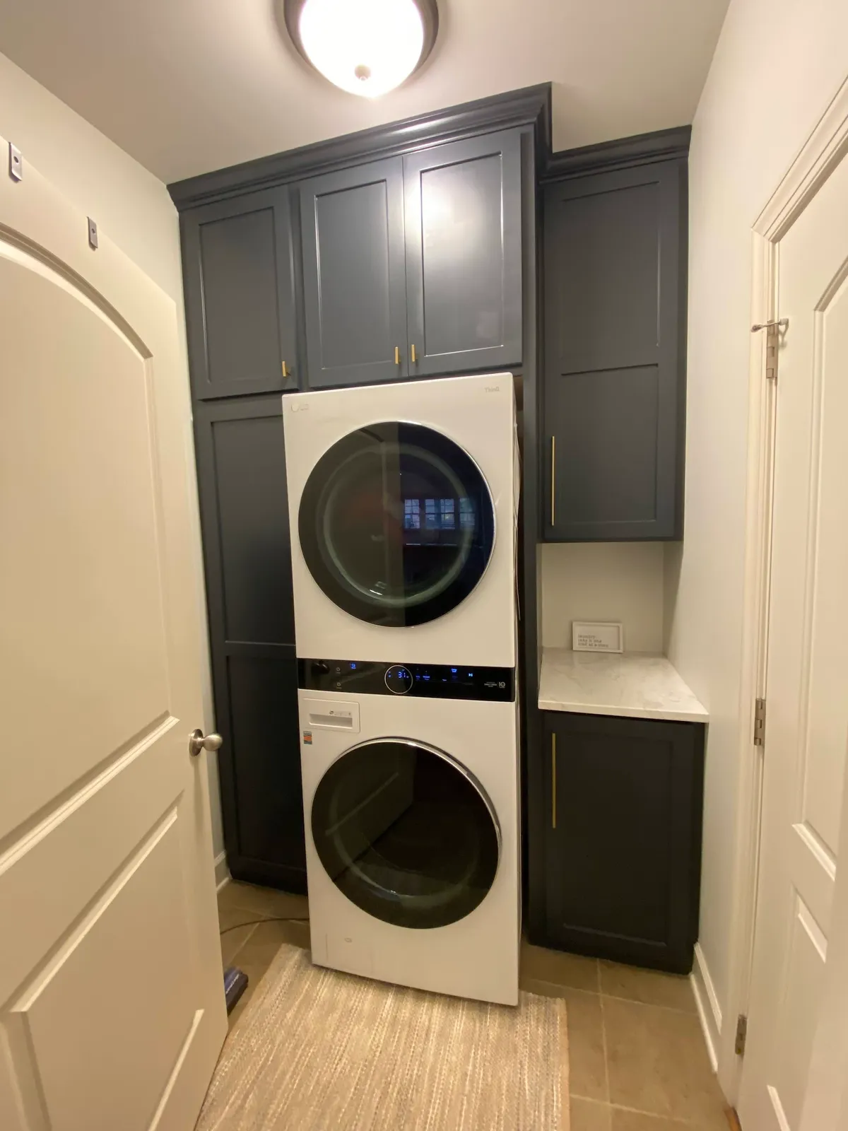 Laundry room with dark gray and white cabinetry and stacked appliances