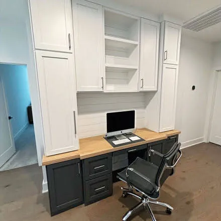 White cabinetry home office with black desk and wall-mounted shelving