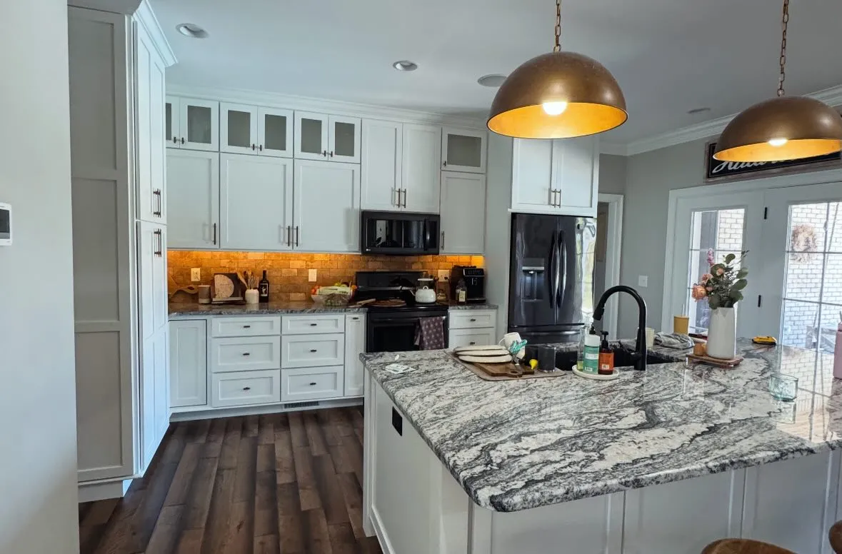 White kitchen with glass-front cabinets, granite island and brass pendants