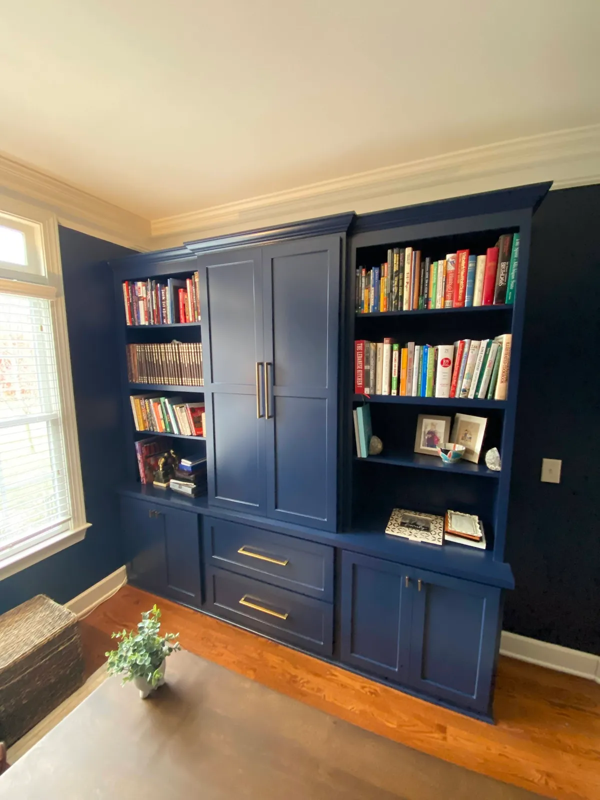 Navy library shelving with brass hardware, glass-front cabinets and sconces
