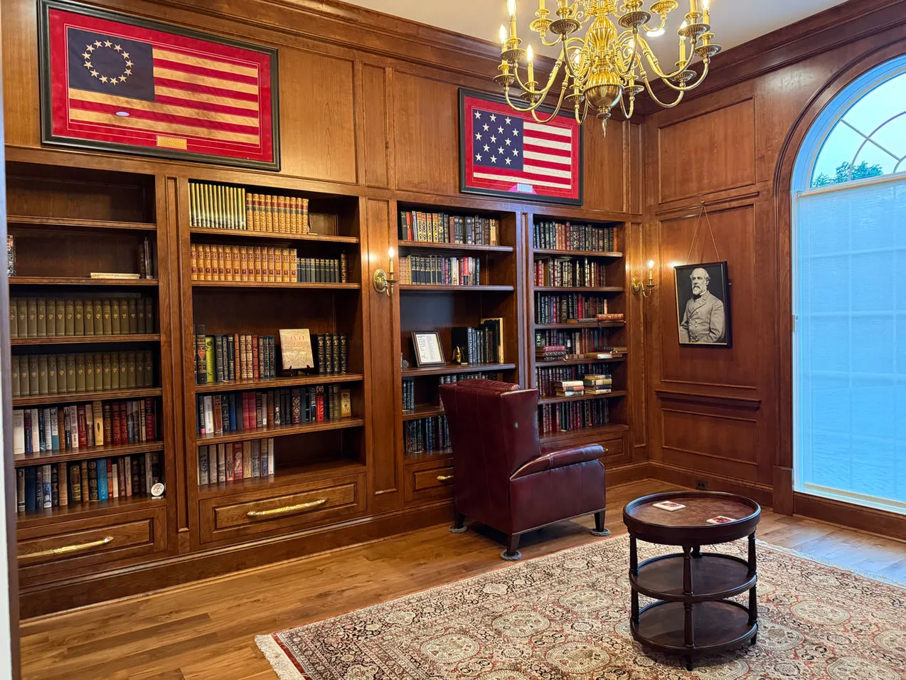 Wood library with leather chair, glass-front shelving and brass chandelier