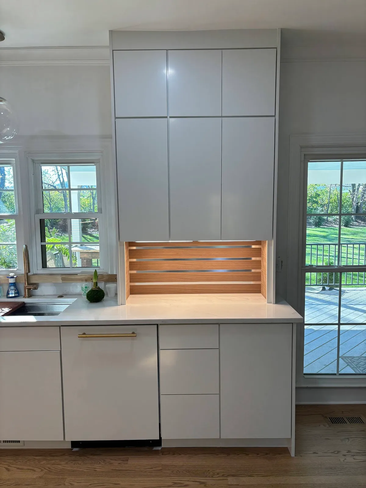 White kitchen with walnut wood hood, upper glass cabinetry and patio doors