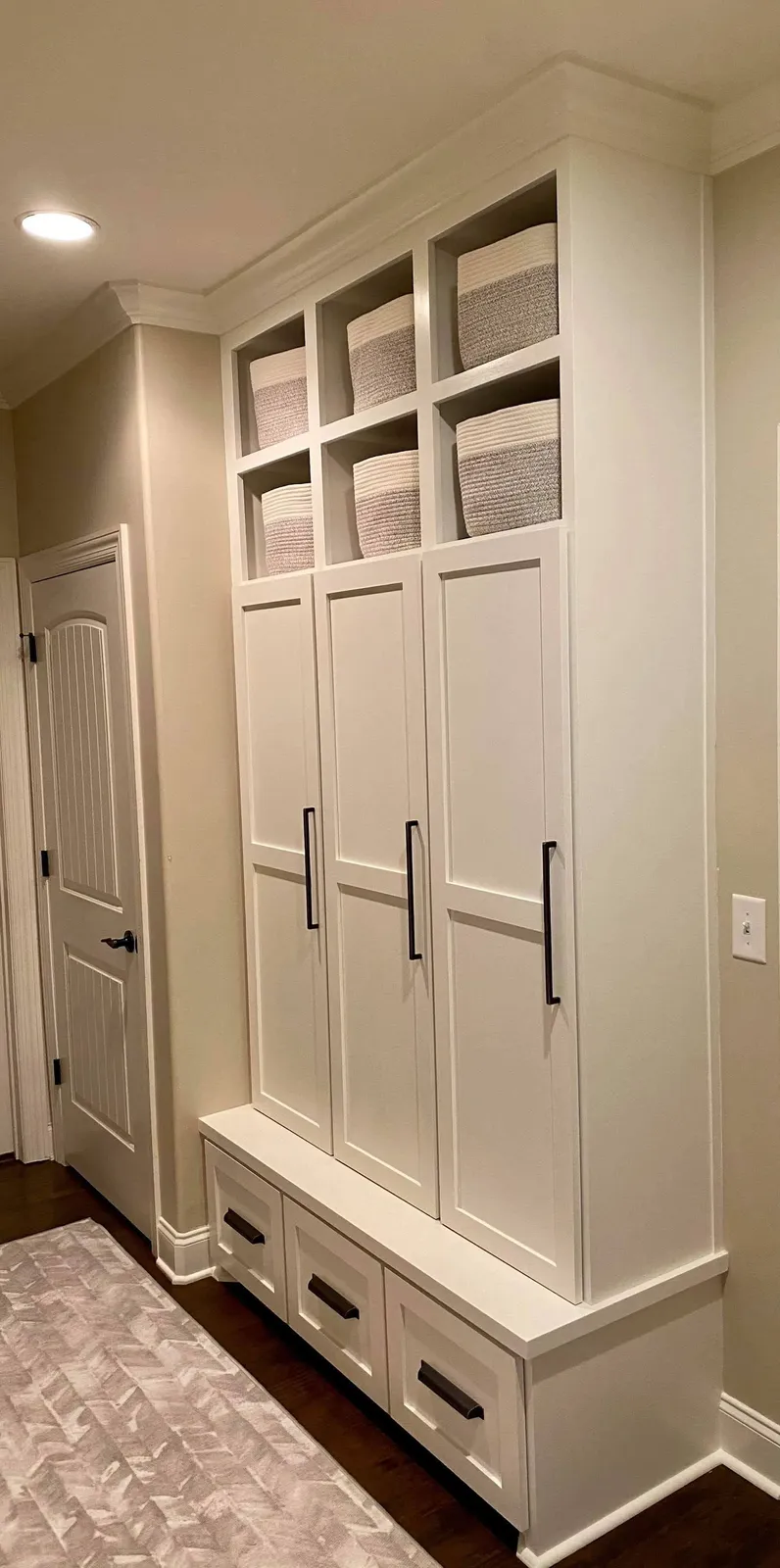 White mudroom with storage cabinets, linen baskets and built-in bench