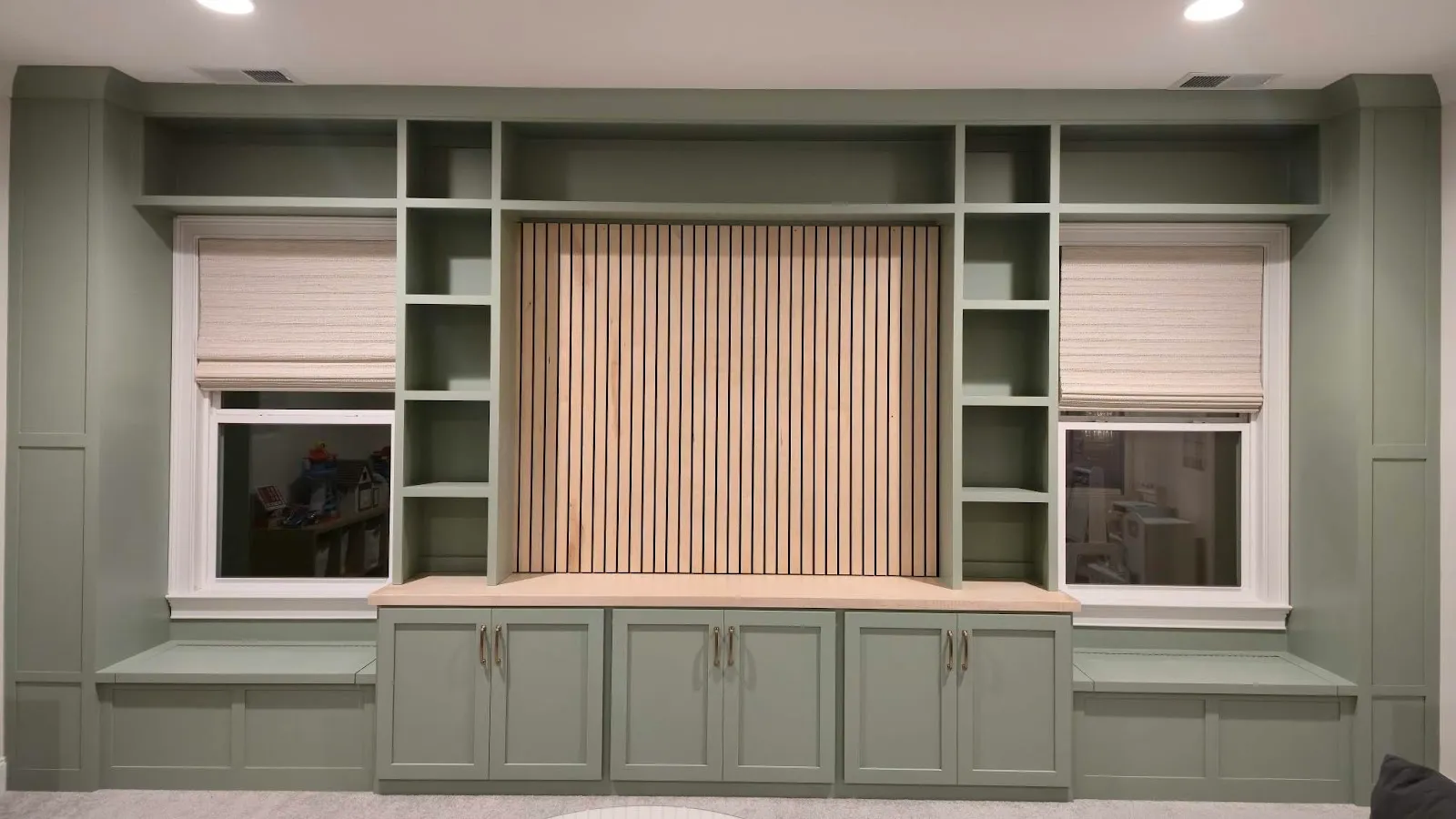 Entertainment wall with sage green cabinetry, floating shelves and window seats
