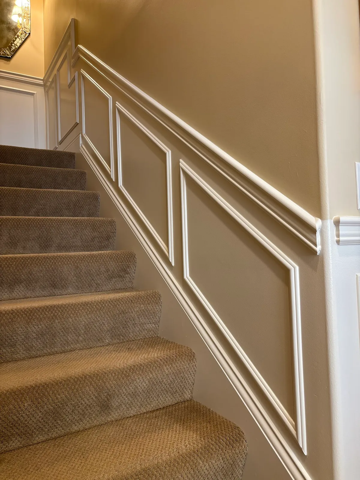 Staircase wainscoting with white trim railings and upper wall paneling