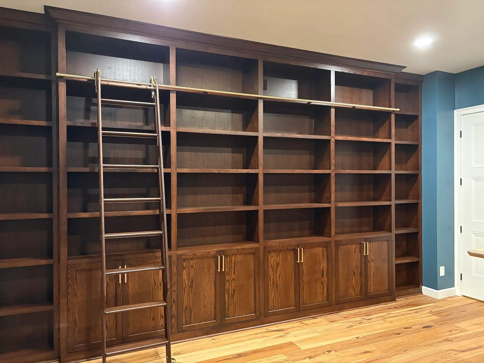 Dark oak library wall shelving with brass ladder rail and built-in storage